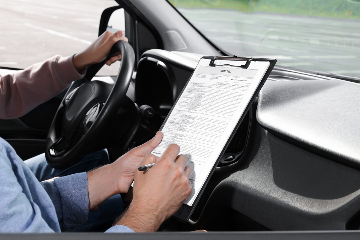 Un élève au volant pendant l'examen pratique du permis de conduire, l'inspecteur remplit la grille d'évaluation